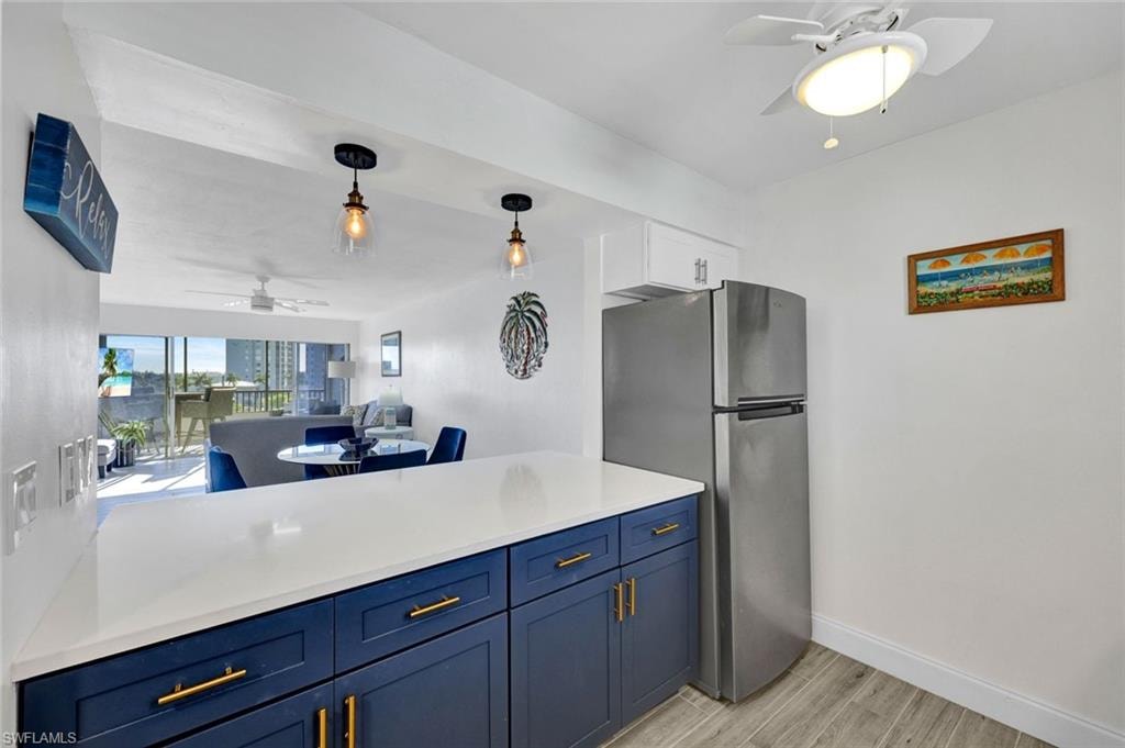 Kitchen with ceiling fan, open floor plan, freestanding refrigerator, blue cabinets, and decorative light fixtures