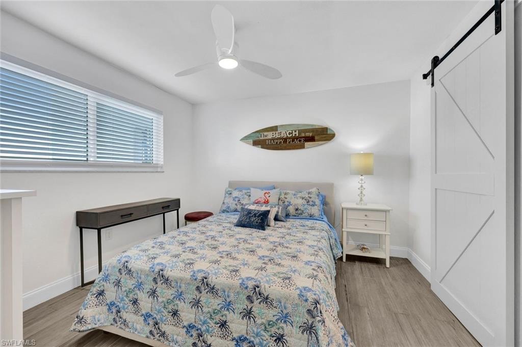 Bedroom with a barn door, light wood finished floors, and ceiling fan
