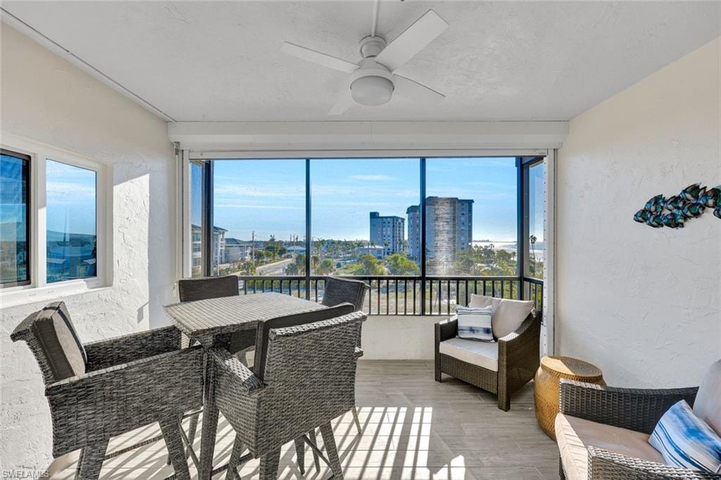 Sunroom with a ceiling fan, a balcony, outdoor dining space, and a city view