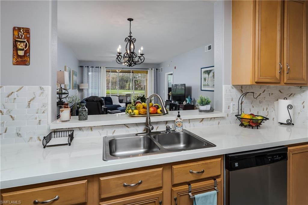 Kitchen with tasteful backsplash, stainless steel dishwasher, light countertops, a chandelier, and wood finish cabinetry