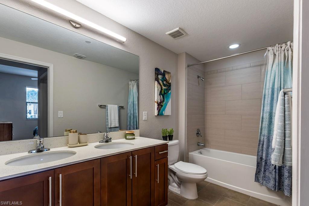 Bathroom featuring shower / bathtub combination with curtain, double vanity, dark tile patterned floors, and recessed lighting