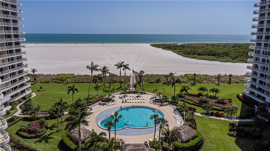 View of swimming pool featuring a patio, a water view, a beach view, and a yard