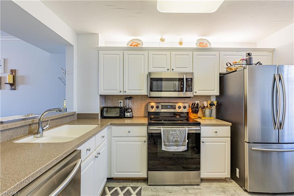 Kitchen featuring stainless steel appliances, white cabinetry, tasteful backsplash, and sink