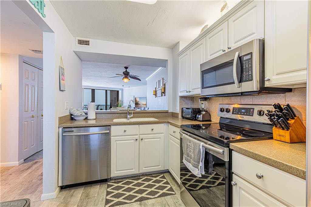 Kitchen with appliances with stainless steel finishes, white cabinetry, light wood-type flooring, ceiling fan, and sink
