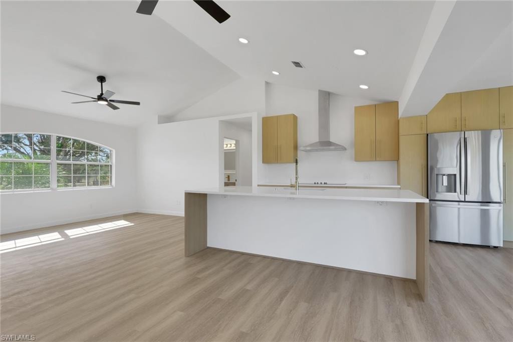 Kitchen featuring stainless steel fridge, modern cabinets, wall chimney exhaust hood, light brown cabinets, and a large island