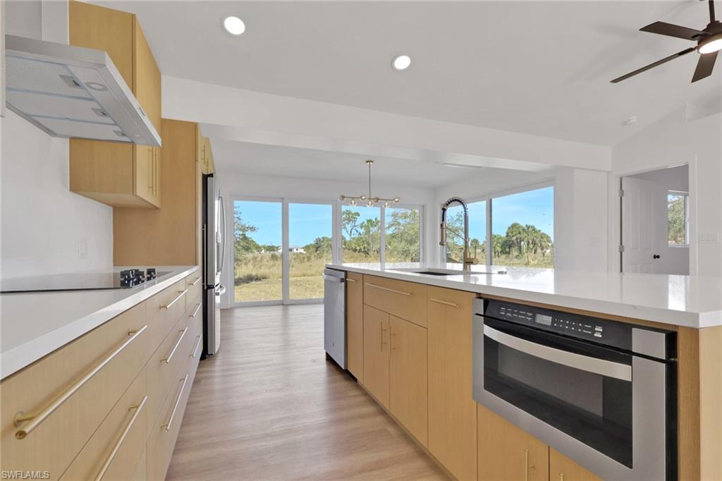 Kitchen featuring light brown cabinets, range hood, a large island, plenty of natural light, and recessed lighting