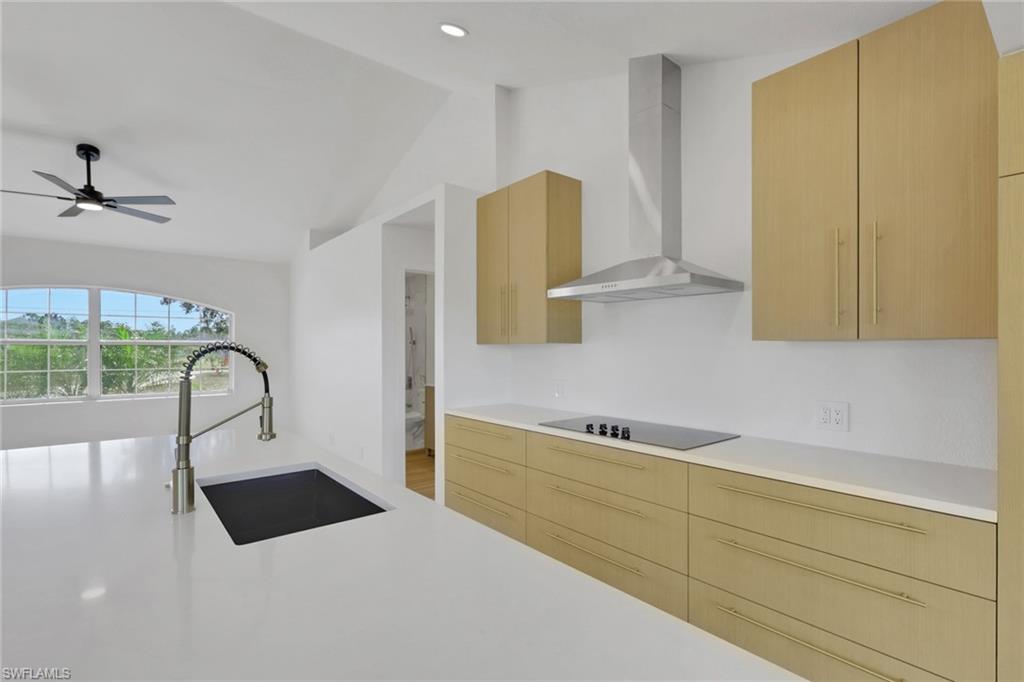 Kitchen with wall chimney range hood, modern cabinets, vaulted ceiling, light brown cabinetry, and black electric stovetop