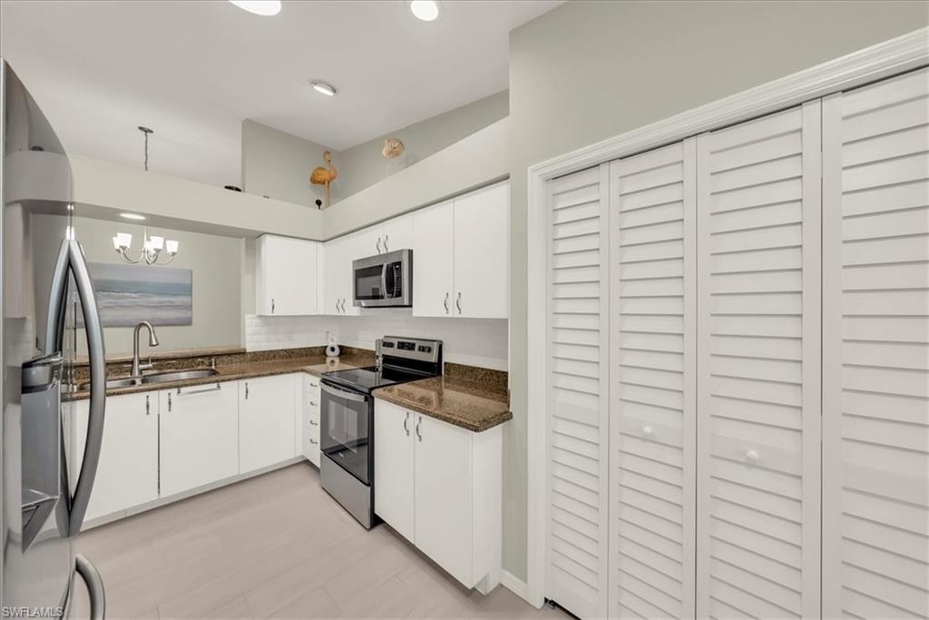 Kitchen featuring appliances with stainless steel finishes, white cabinets, dark stone counters, and a chandelier