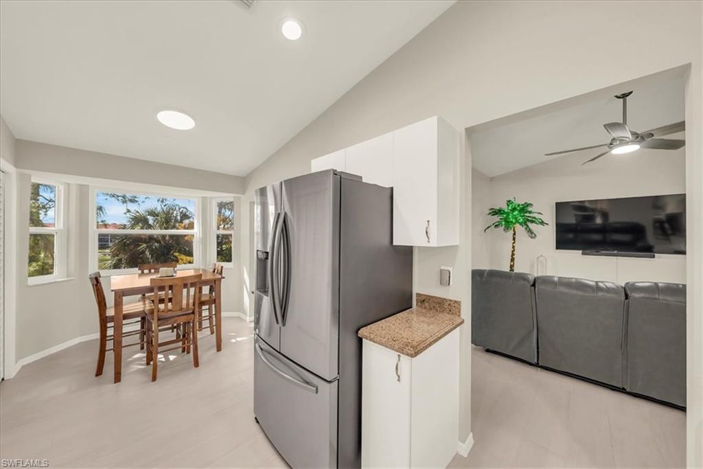 Kitchen with vaulted ceiling, stainless steel fridge with ice dispenser, white cabinetry, open floor plan, and light stone counters