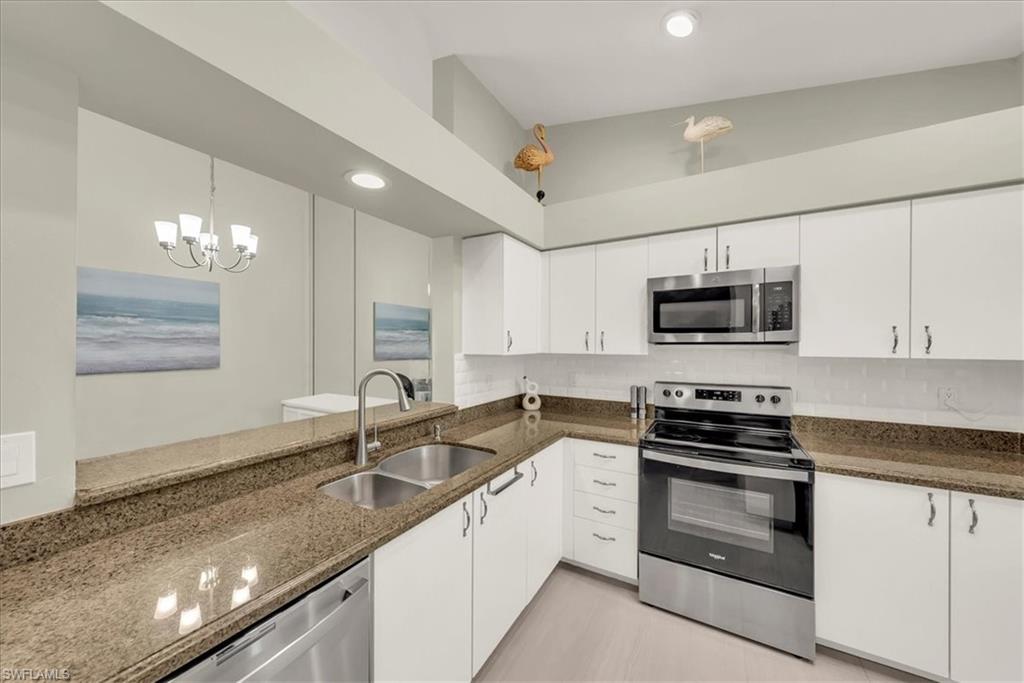 Kitchen with stainless steel appliances, dark stone countertops, white cabinetry, decorative light fixtures, and recessed lighting