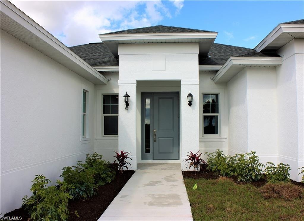 Property entrance featuring a shingled roof and stucco siding