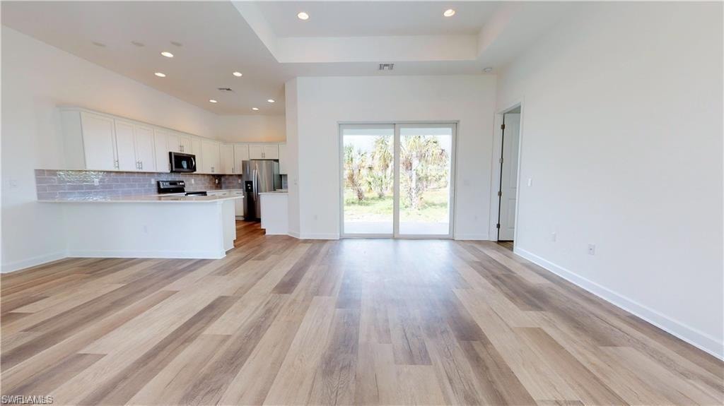 Kitchen featuring open floor plan, light countertops, white cabinets, backsplash, and appliances with stainless steel finishes