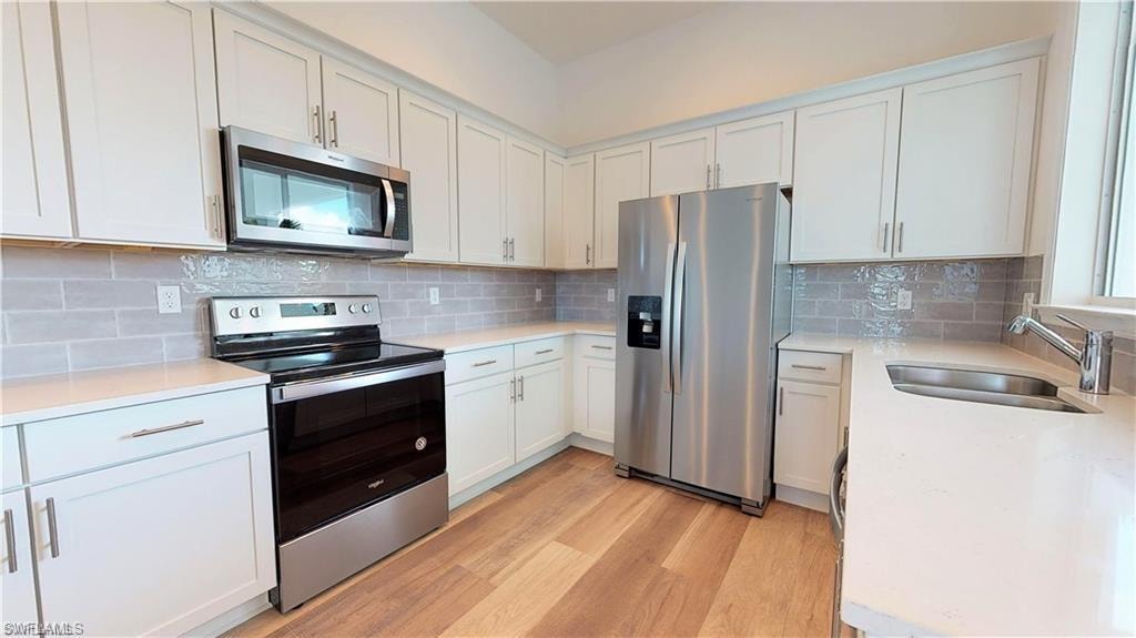 Kitchen with stainless steel appliances, white cabinetry, light wood-style floors, and light stone countertops