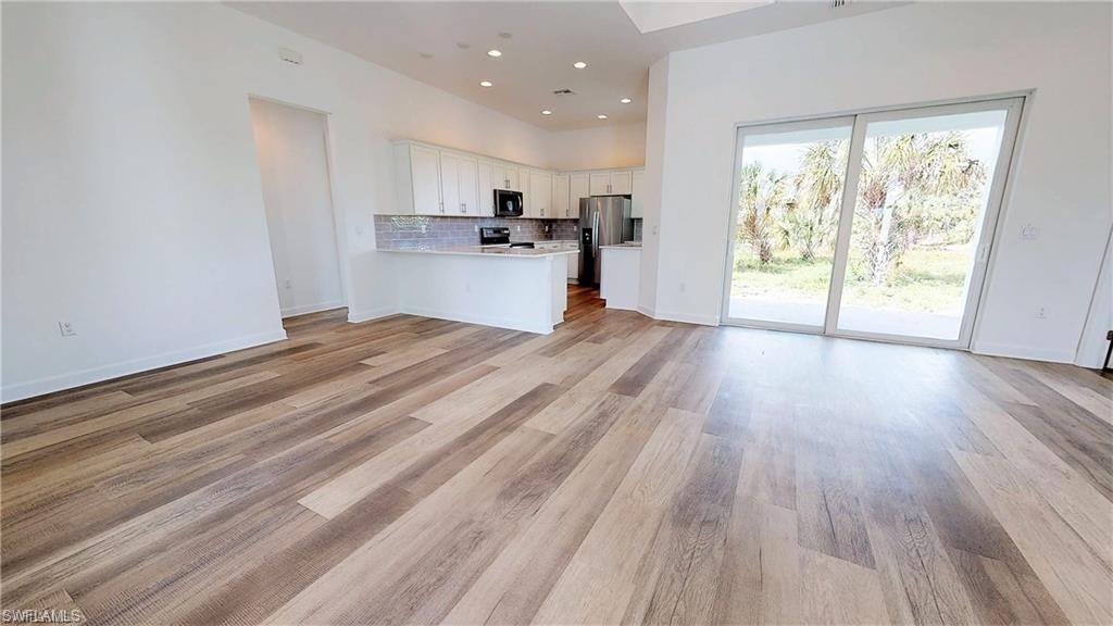 Kitchen with open floor plan, white cabinetry, a peninsula, light wood-style flooring, and stainless steel appliances