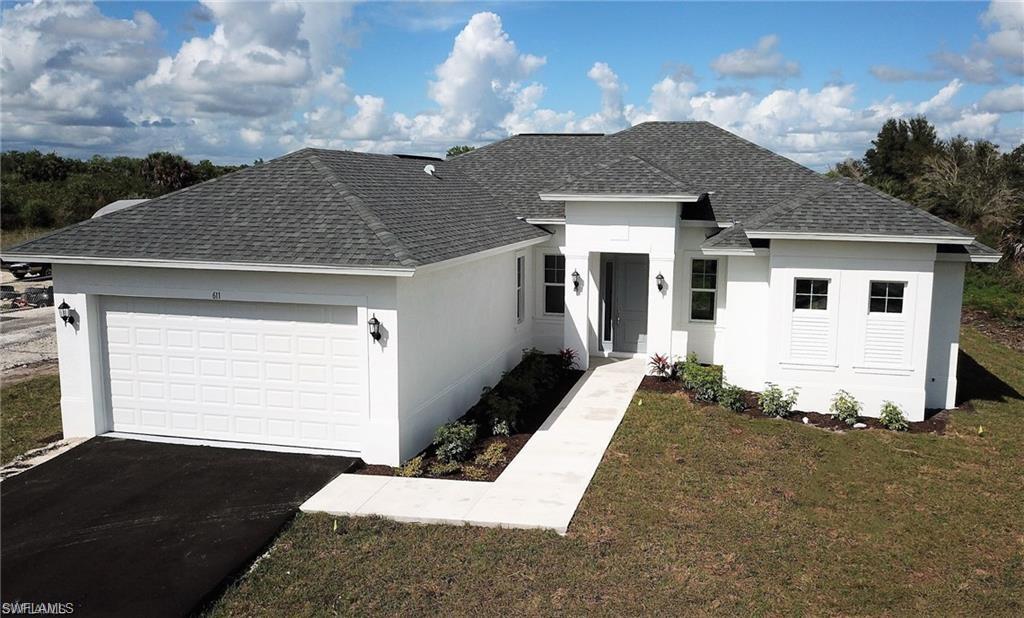 View of front of house with a shingled roof, an attached garage, asphalt driveway, a front lawn, and stucco siding