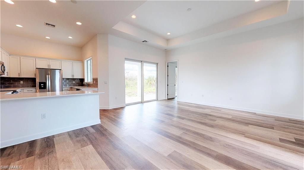 Kitchen with stainless steel appliances, white cabinetry, tasteful backsplash, open floor plan, and a tray ceiling