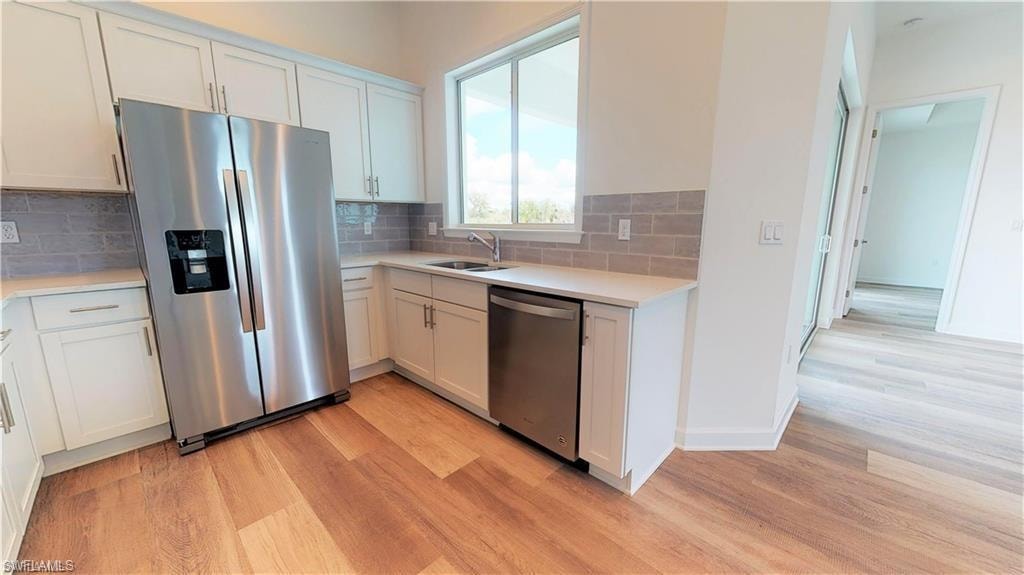 Kitchen with appliances with stainless steel finishes, light wood-type flooring, and white cabinets