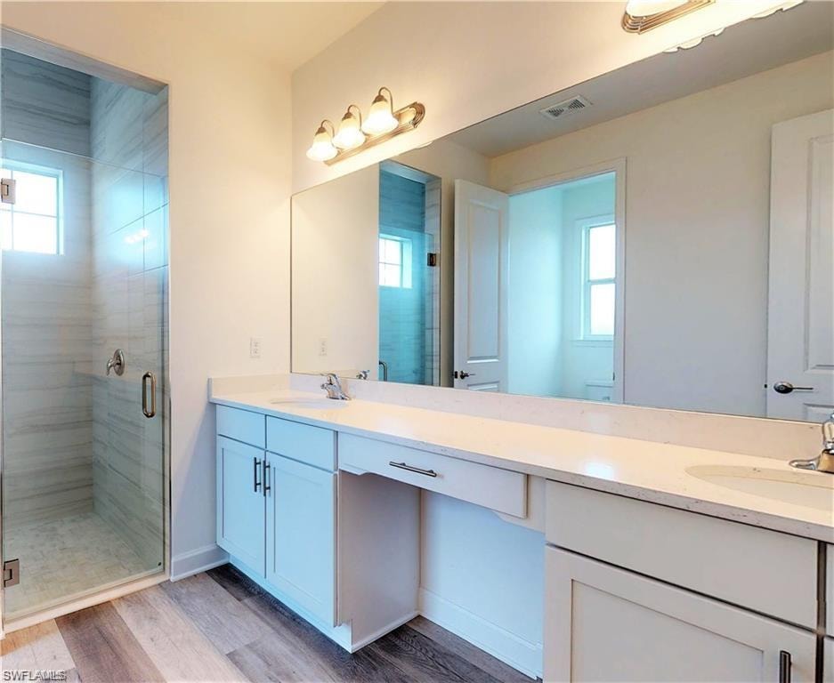 Bathroom featuring a stall shower, double vanity, and light wood-type flooring