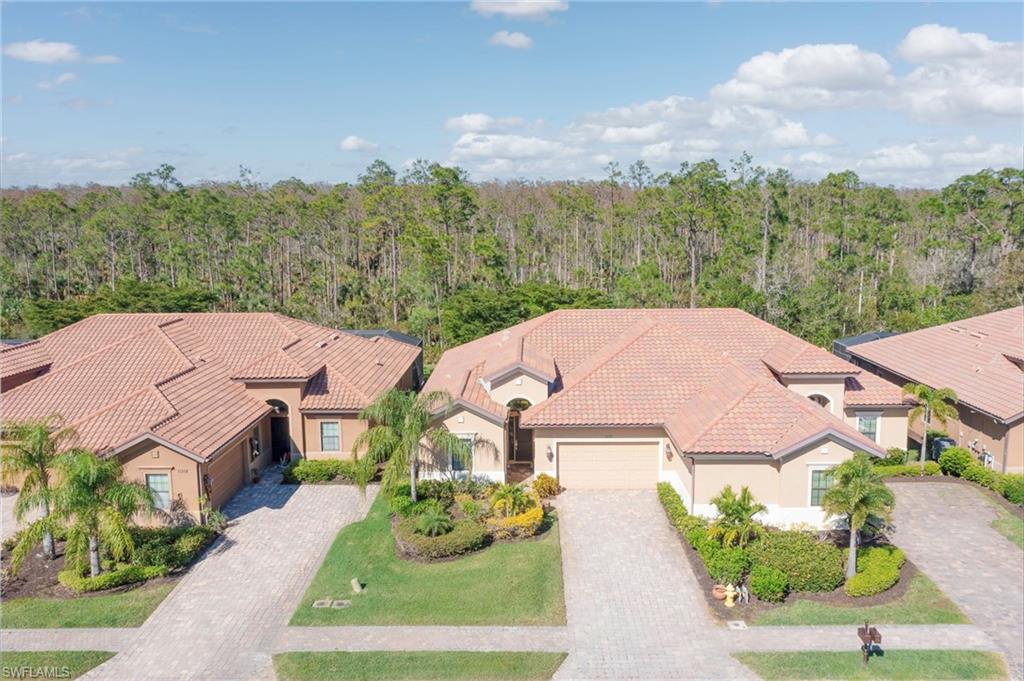 View of front of property with stucco siding, an attached garage, driveway, a view of trees, and a tile roof