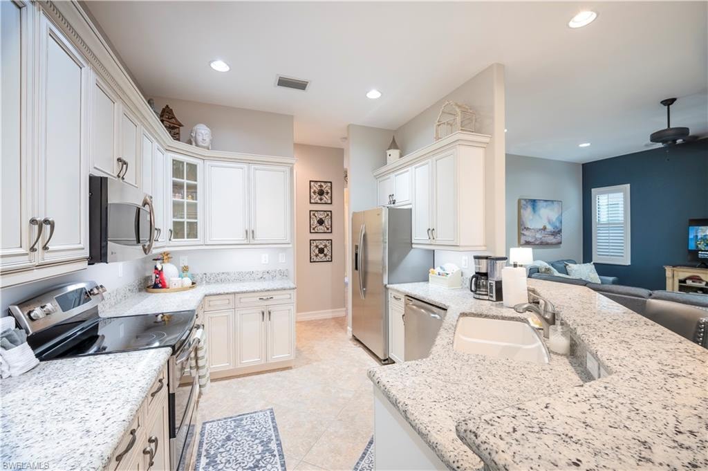 Kitchen with stainless steel appliances, open floor plan, light stone countertops, glass insert cabinets, and recessed lighting