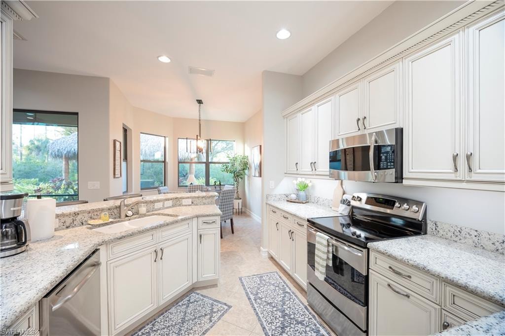 Kitchen featuring stainless steel appliances, light stone counters, healthy amount of natural light, and light tile patterned floors