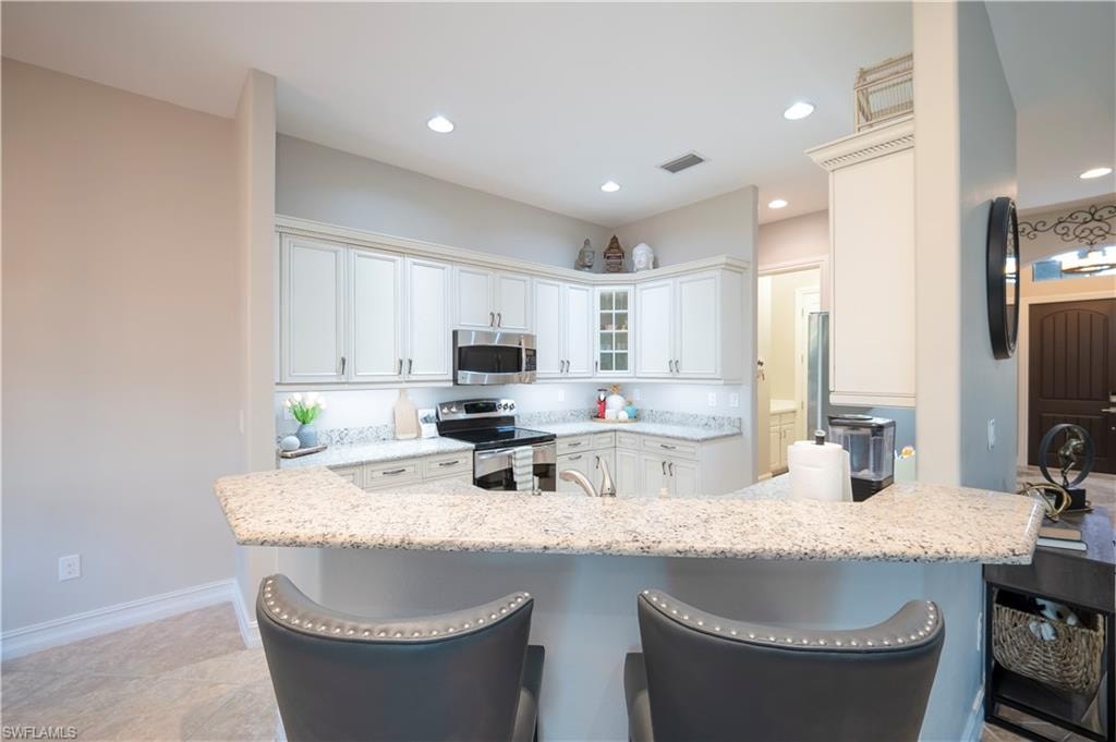 Kitchen with glass insert cabinets, a kitchen bar, white cabinetry, stainless steel appliances, and light stone counters