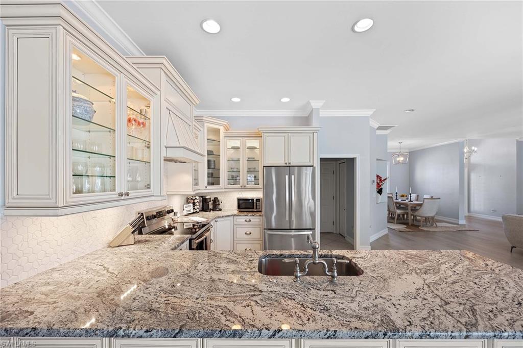 Kitchen with stainless steel appliances, ornamental molding, light stone counters, glass insert cabinets, and premium range hood