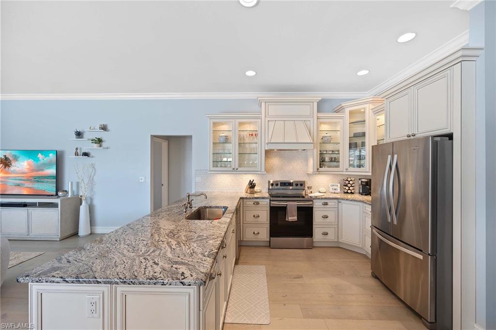 Kitchen featuring light stone countertops, stainless steel appliances, a peninsula, glass insert cabinets, and crown molding