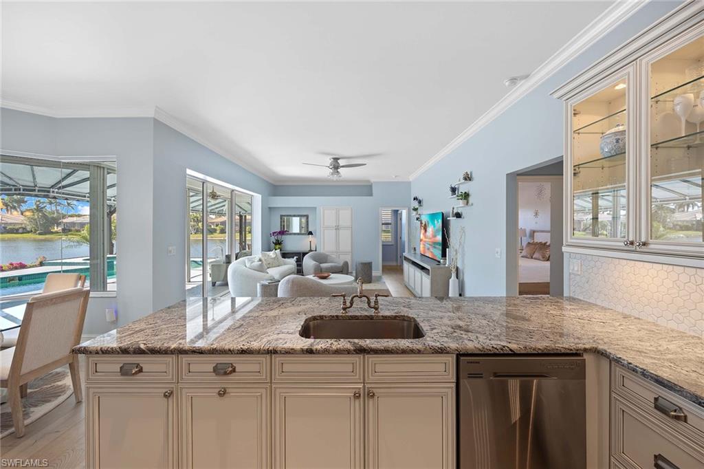 Kitchen with stainless steel dishwasher, light stone countertops, open floor plan, ornamental molding, and a peninsula
