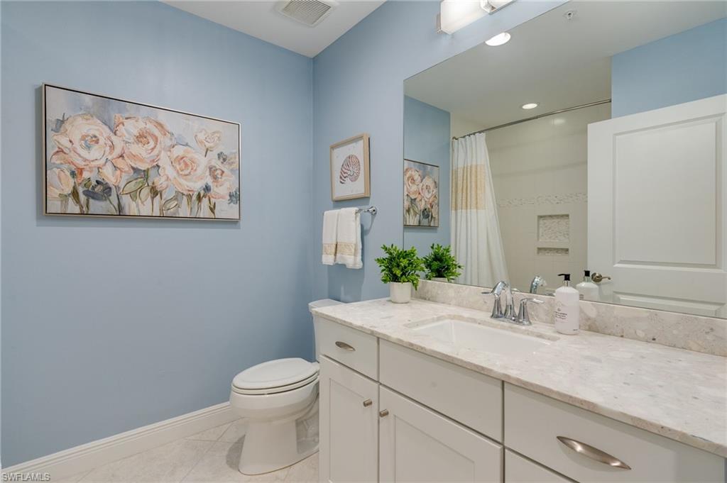 Guest bathroom features neutral colors, a custom raised shower head to accommodate a tall person, and a corresponding oversized custom length shower curtain and recessed lighting
