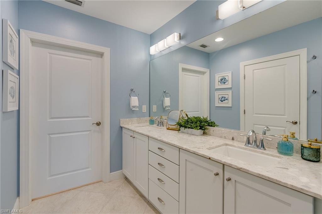 Primary bathroom featuring a double sink vanity and bright vanity lights as well as flush ceiling lighting.  Ample storage and lower cabinets feature pull out stainless organizers.
