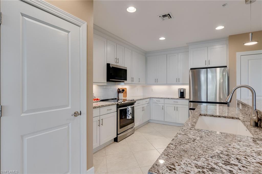 Kitchen featuring stainless steel appliances, light stone countertops, white cabinetry, new neutral backsplash, and woooden pull out trays in lower cabinets.