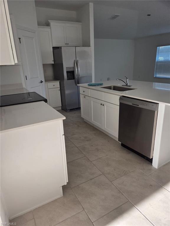 Kitchen with white cabinets, appliances with stainless steel finishes, a center island with sink, and light tile patterned floors