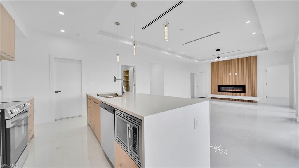 Kitchen with a raised ceiling, modern cabinets, open floor plan, a fireplace, and appliances with stainless steel finishes