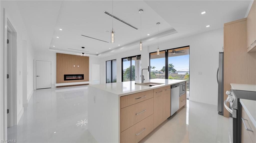 Kitchen featuring light brown cabinetry, hanging light fixtures, open floor plan, a tray ceiling, and recessed lighting
