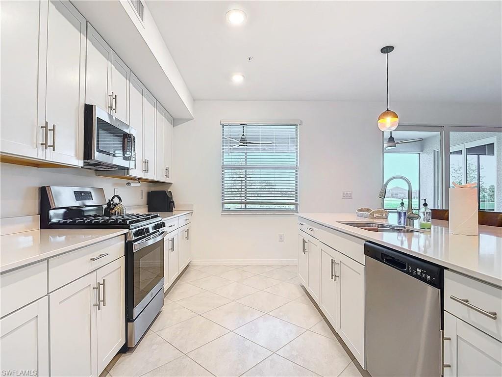 Kitchen with pendant lighting, sink, light tile patterned floors, white cabinetry, and stainless steel appliances