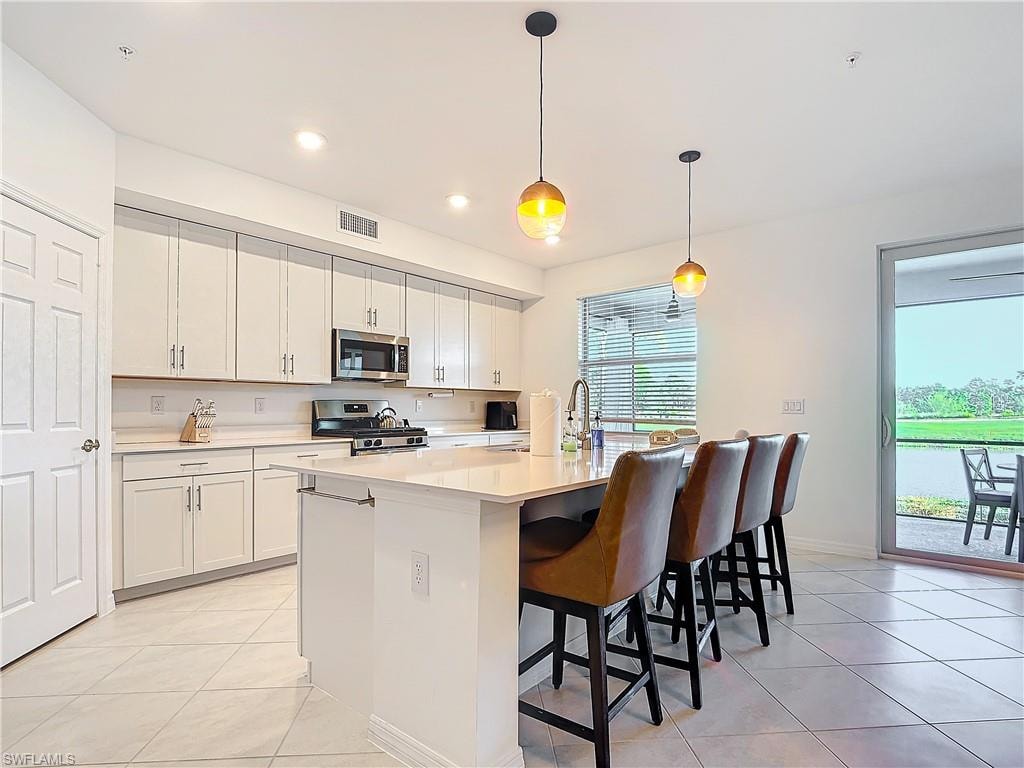 Kitchen featuring a center island with sink, pendant lighting, white cabinetry, and stainless steel appliances
