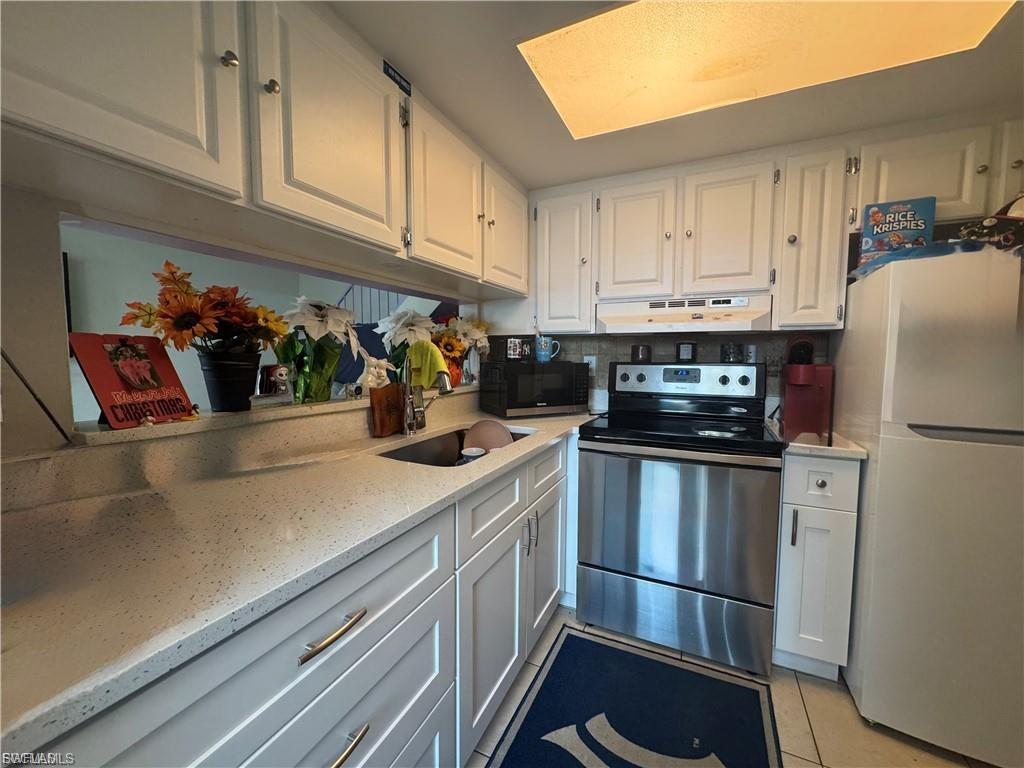 Kitchen featuring stainless steel electric range oven, freestanding refrigerator, white cabinets, and light stone countertops