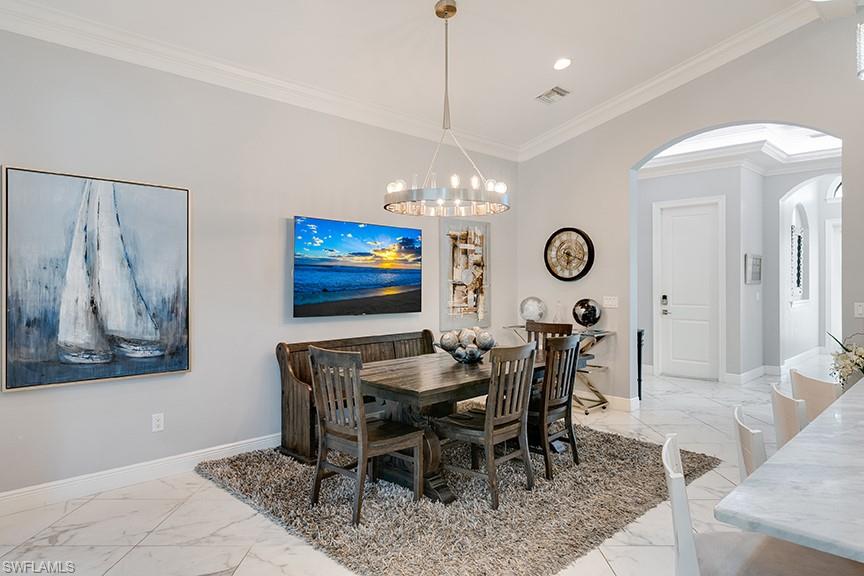 Dining area featuring arched walkways, light marble finish floors, crown molding, and hanging lights