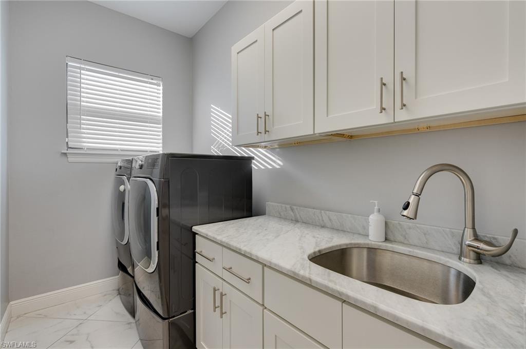 Laundry area featuring independent washer and dryer, cabinet space, and light marble finish flooring