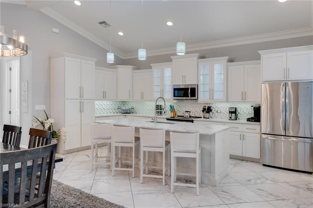 Kitchen with stainless steel appliances, a kitchen bar, light marble finish floors, lofted ceiling, and light stone counters
