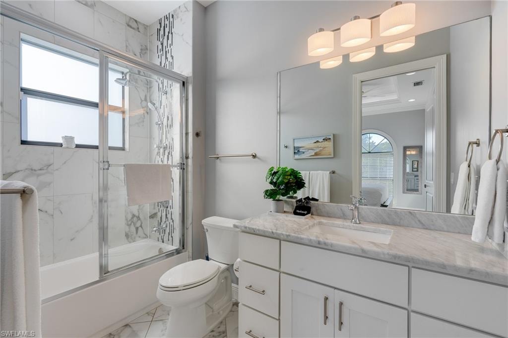 Bathroom featuring bath / shower combo with glass door, vanity, and light marble finish floors