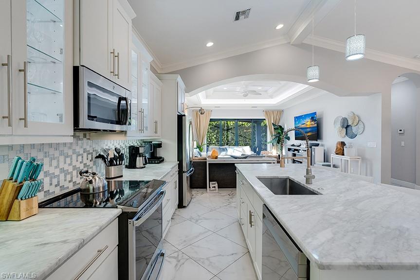 Kitchen featuring white cabinets, stainless steel appliances, a kitchen island with sink, glass fronted cabinets, and crown molding