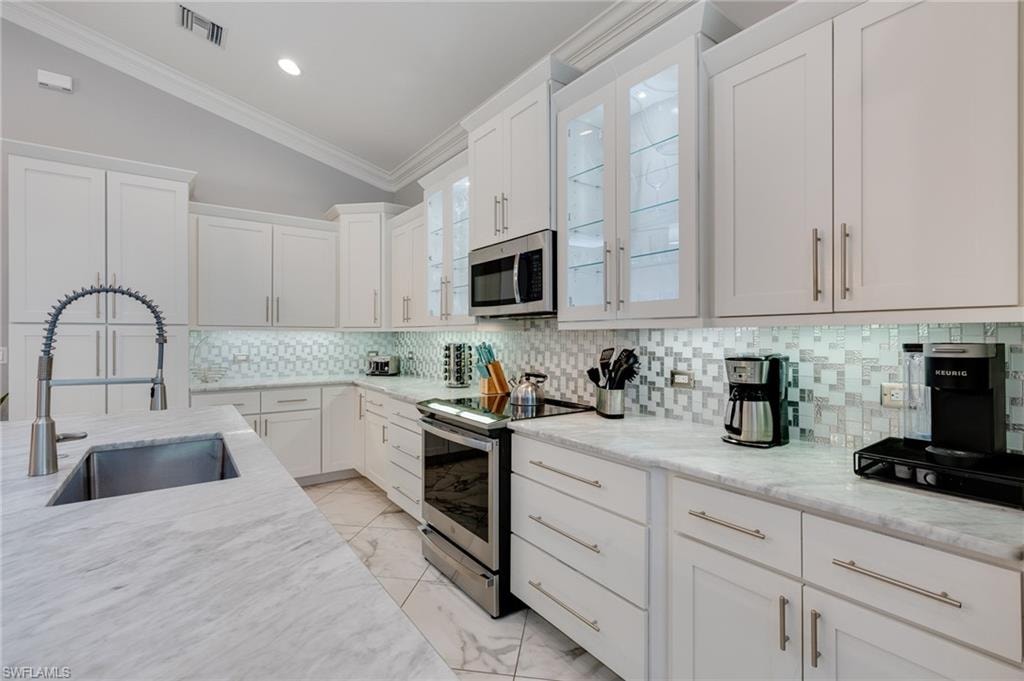 Kitchen with vaulted ceiling, stainless steel appliances, tasteful backsplash, white cabinetry, and light stone counters