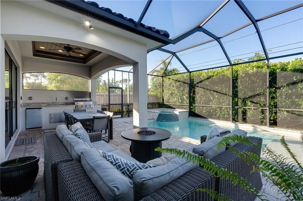 View of patio / terrace with an outdoor kitchen and area to lounge, ceiling fan, glass enclosure, a pool with connected hot tub, and a sunroom