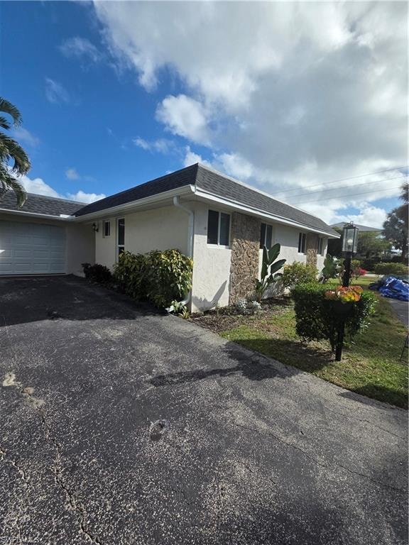 View of side of home with stucco siding, an attached garage, roof with shingles, and driveway