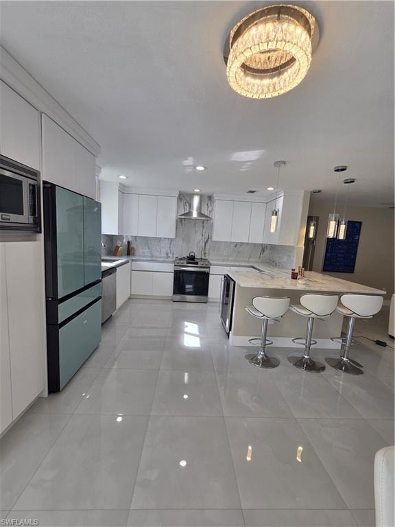 Kitchen with white cabinetry, refrigerator, a kitchen bar, stainless steel range, and hanging light fixtures