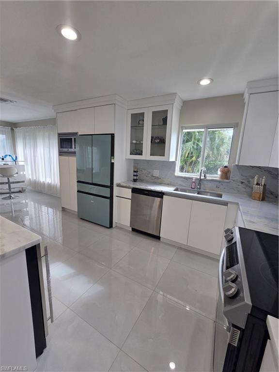 Kitchen with white cabinetry, range, fridge, dishwasher, and light stone counters