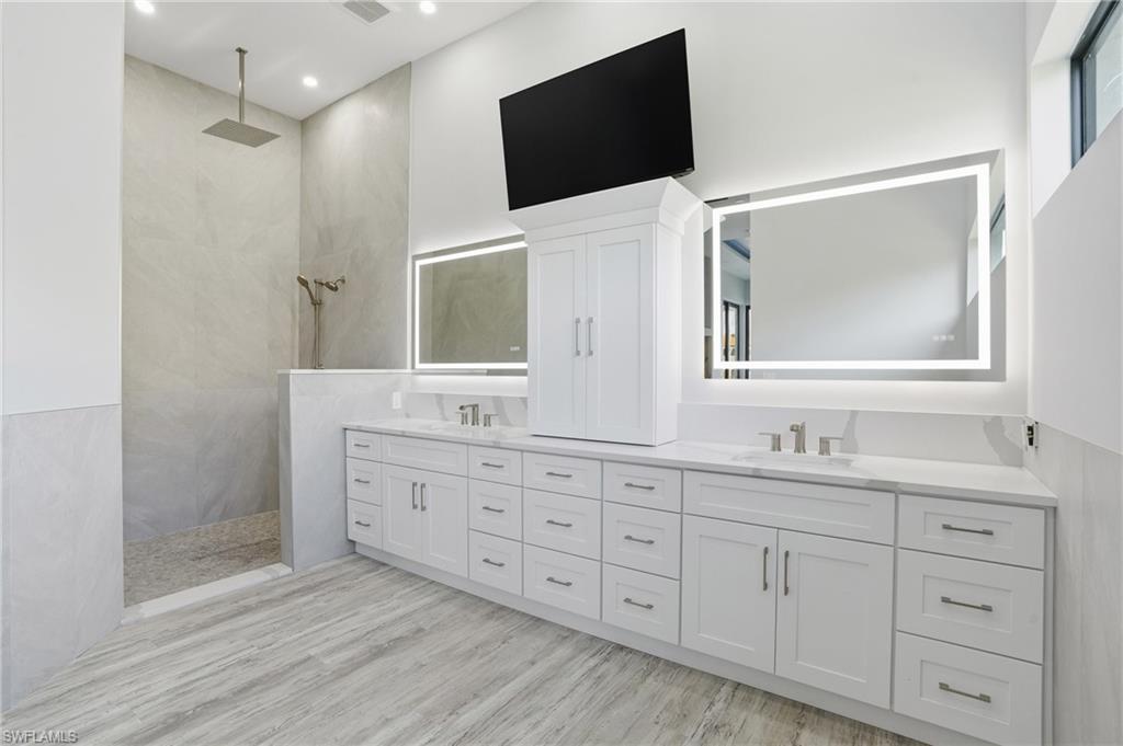 Full bath with double vanity, walk in shower, and light wood-style floors