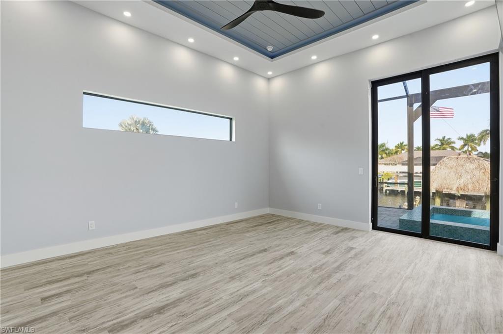 Spare room featuring light wood finished floors, ceiling fan, plenty of natural light, a raised ceiling, and recessed lighting